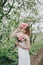 Beautiful bride in a wedding dress with bouquet and roses wreath posing in a green garden