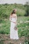 Beautiful bride in a wedding dress with bouquet and roses wreath posing in a green garden