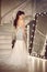 Beautiful Bride in wedding dress posing by staircase in luxurious interior. Elegant brunette woman in long gown standing by