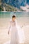 Beautiful bride in a white chiffon dress with sleeves and lace on the shore of Lake Lago di Braies in Italy. Destination