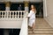 A beautiful bride in a white dress and with a bouquet climbs the steps to the groom in a luxurious suite