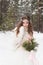 Beautiful bride in a white dress with a bouquet in a snow-covered winter forest. Portrait of the bride in nature.