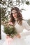 Beautiful bride in a white dress with a bouquet in a snow-covered winter forest. Portrait of the bride in nature.