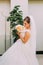 Beautiful bride in white dress posing indoors with wedding bouquet of pale pink and yellow roses