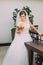 Beautiful bride in white dress standing near the baluster holding wedding bouquet of pale pink roses
