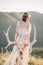 A beautiful bride a woman holds a moose skull on her hand and stands with her back to the mountains