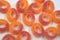 Beautiful and bright colored sweets in the form of orange and red doughnuts in sugar powder, arranged on a white matte background.