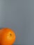 Beautiful bright orange orange with shiny thick peel on a gray background. Fruit on the bottom right. Free space for text. Healthy