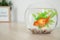 Beautiful bright small goldfish in round glass aquarium on wooden table. Space for text