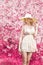 Beautiful bright smiling soft sweet girl with long blond curly hair wearing a hat with large fields in the summer pink sundress