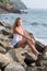 Beautiful brooding mature tourist woman sitting on rock asian beach  looking down