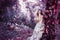 Beautiful brown-haired woman in a long white dress, with a wreath of lavender on her head, is in the fairy forest.