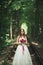 Beautiful brunette bride in elegant white dress holding bouquet posing neat trees