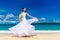 Beautiful brunette bride in white wedding dress with big long white train and with wedding bouquet stand on shore sea. Tropical s