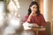 Beautiful brunette business lady in modern gems and fashionable burgundy dress having a lunch in cafe. Woman sits by the