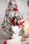 Beautiful brunette in Christmas interior. Elegant winter woman in white dress present gift box with red ribbon bow, pretty lady in