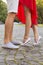 Beautiful brunette couple in love kissing on a date in the park, close up of their legs. She in red dress, on a tiptoes. He in sh