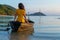 Beautiful brunette girl in a yellow dress sits in an old wooden boat overlooking a deserted tropical island. Romance at sea