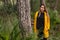 Beautiful brunette-haired woman in yellow coat posing in the forest, near a pine tree. Nature and fashion