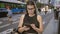 Beautiful brunette hispanic woman in glasses, engrossed in serious smartphone conversation on madrid\\\'s urban streets