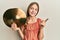 Beautiful brunette little girl holding golden cymbal plates smiling happy pointing with hand and finger to the side