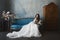 and beautiful brunette model girl in stylish and fashionable lace wedding dress with naked shoulders sits on the antique sofa