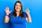 Beautiful brunette plus size woman wearing casual blue t shirt showing and pointing up with fingers number eight while smiling