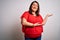 Beautiful brunette plus size woman wearing casual red t-shirt over isolated white background Inviting to enter smiling natural