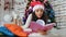 Beautiful brunette in a Santa hat is lying under a brightly decorated Christmas tree and reading a book. Crimson and