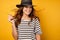 Beautiful brunette in a striped T-shirt and wicker hat with frolic hair is standing on a yellow background, looking to