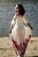Beautiful brunette stylish bride in unique embroidery dress in a sunny lake, concept of happiness