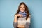 A beautiful brunette in a sweater and a blue knitted scarf stands on a blue background and smiles into the frame.
