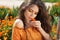 Beautiful brunette woman with colored makeup smelling flower, over marigold flowers field