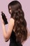 Beautiful brunette woman with curls and classic make-up in a black dress with a bottle of shampoo in hands. Beauty face.