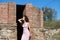Beautiful brunette woman with curly hair among the ruins of an old abandoned building. The woman is dressed in an elegant pink and