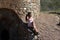 beautiful brunette woman with curly hair sitting on a wall of the ruins of an old abandoned building. The woman is dressed in an