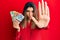 Beautiful brunette woman holding australian dollars doing stop sing with palm of the hand