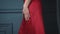 Beautiful brunette woman lady in a silk red dress evening make-up leans against a blue wall to bask in a luxurious life glamorous