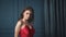 Beautiful brunette woman lady in a silk red dress evening make-up leans against a blue wall to bask in a luxurious life glamorous