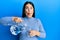 Beautiful brunette woman pouring water in glass making fish face with mouth and squinting eyes, crazy and comical