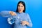 Beautiful brunette woman pouring water in glass in shock face, looking skeptical and sarcastic, surprised with open mouth