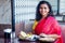 Beautiful brunette woman in red sari eating with appetite traditional thali wirh rise,curd,dal in Goa restaurant masala