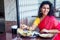 Beautiful brunette woman in red sari eating with appetite traditional thali wirh rise,curd,dal in Goa restaurant masala