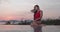 Beautiful brunette woman in red swimsuit posing by outdoor pool over sunset sky