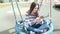 Beautiful brunette woman is swinging on empty webbed swing, loking at social media on mobile phone.