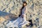 Beautiful brunette woman in translucent beach cover up with leopard fur coat and black boots posing on sandy beach at sunset.