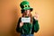 Beautiful brunette woman wearing hat with clover holding banner with go green message doing ok sign with fingers, excellent symbol