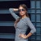 Beautiful brunette young woman in nice striped dress, sunglasses. Posing on urban background. Fashion Photo