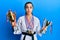 Beautiful brunette young woman wearing karate fighter uniform and medals holding trophy puffing cheeks with funny face