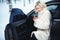 Beautiful business woman in luxurious white fur coat drinking hot coffee on snowy winter day sitting in her car